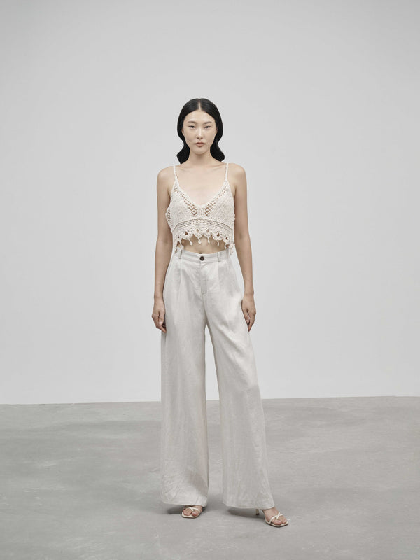 Woman wearing a white lace top and light-colored pants against a plain background
