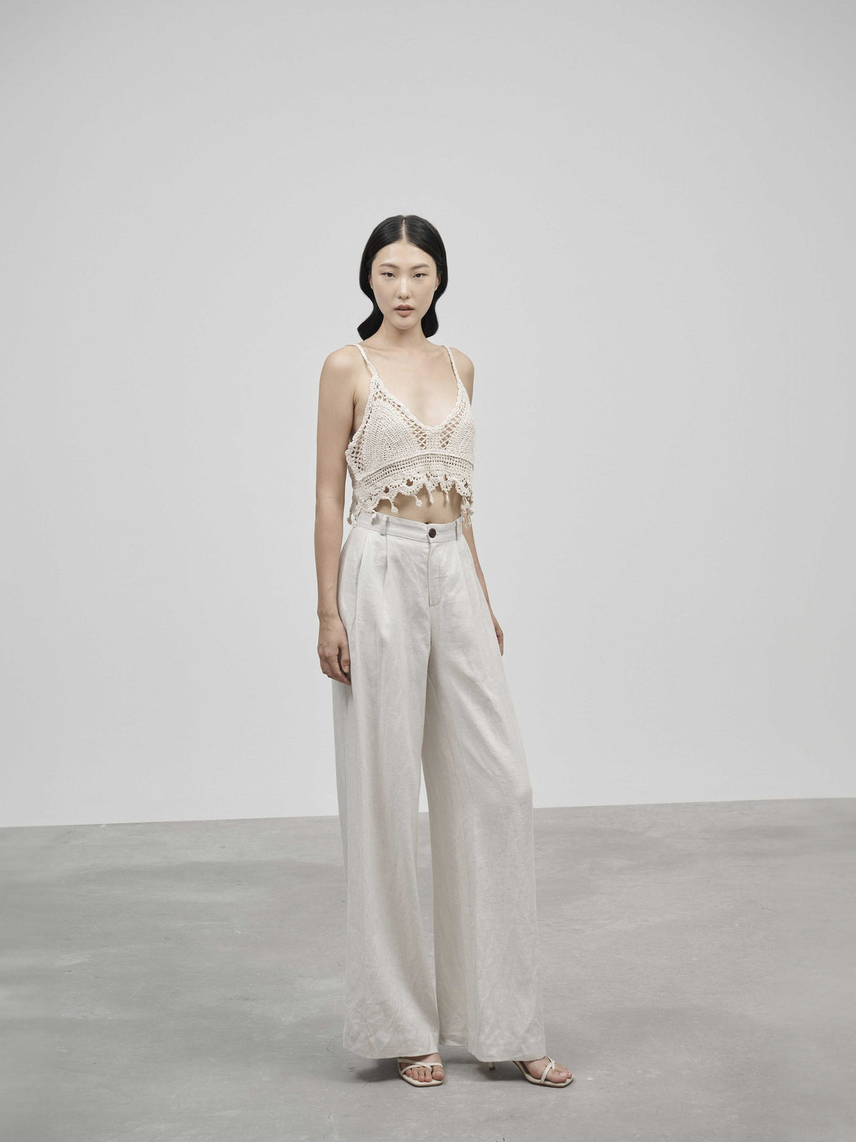 Woman wearing a white lace top and light-colored pants against a plain background — view 3