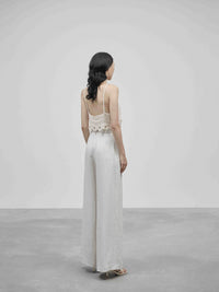 Woman wearing a white outfit with a lace top and wide-leg pants on a plain background — view 2