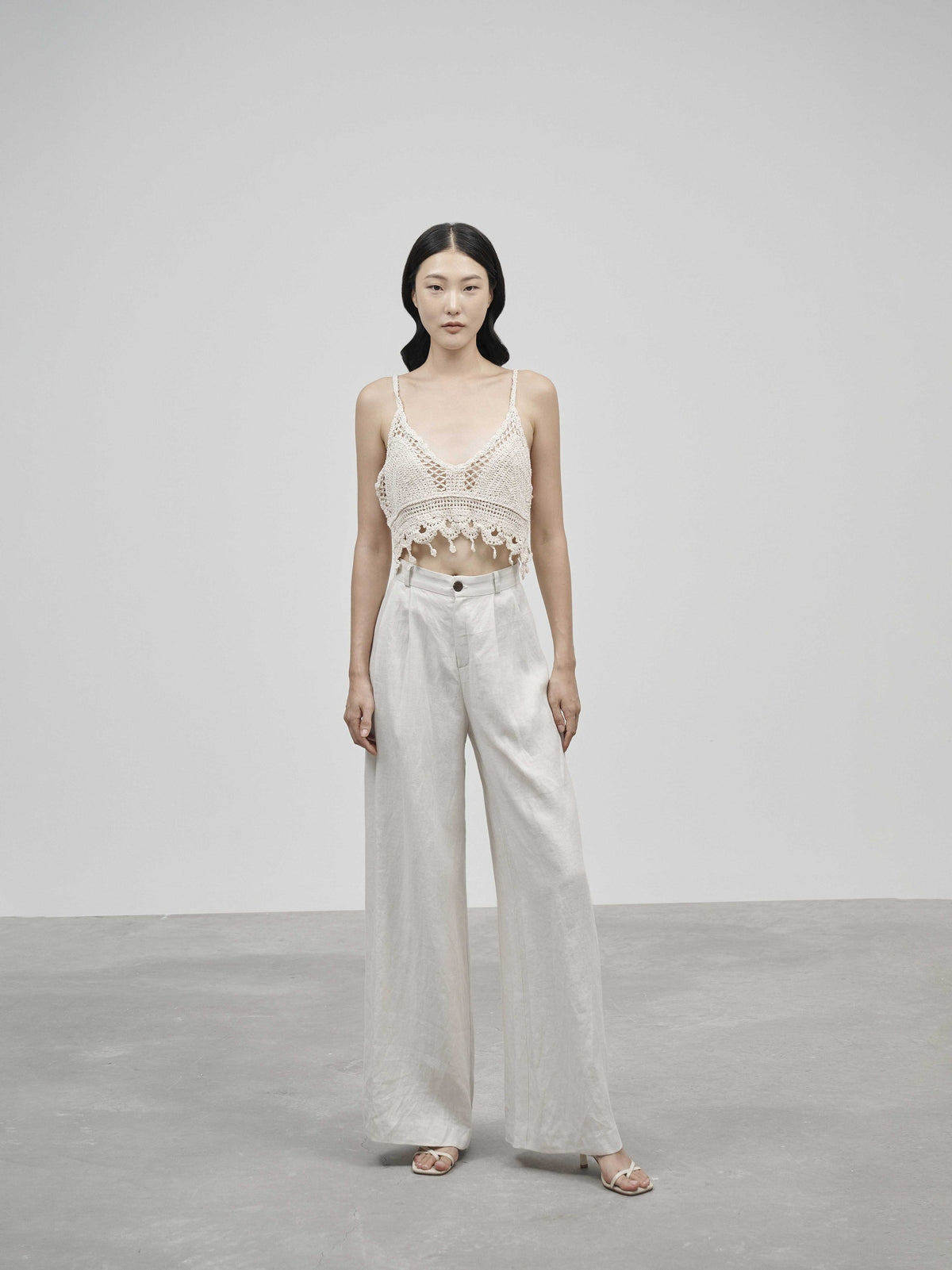 Woman wearing a white lace top and light-colored pants against a plain background — view 1