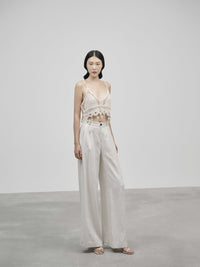 Woman wearing a white lace top and light-colored pants against a plain background — view 3